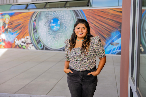 Betsaida Rodriguez, a CSUMB student, standing and posing in front of a mural