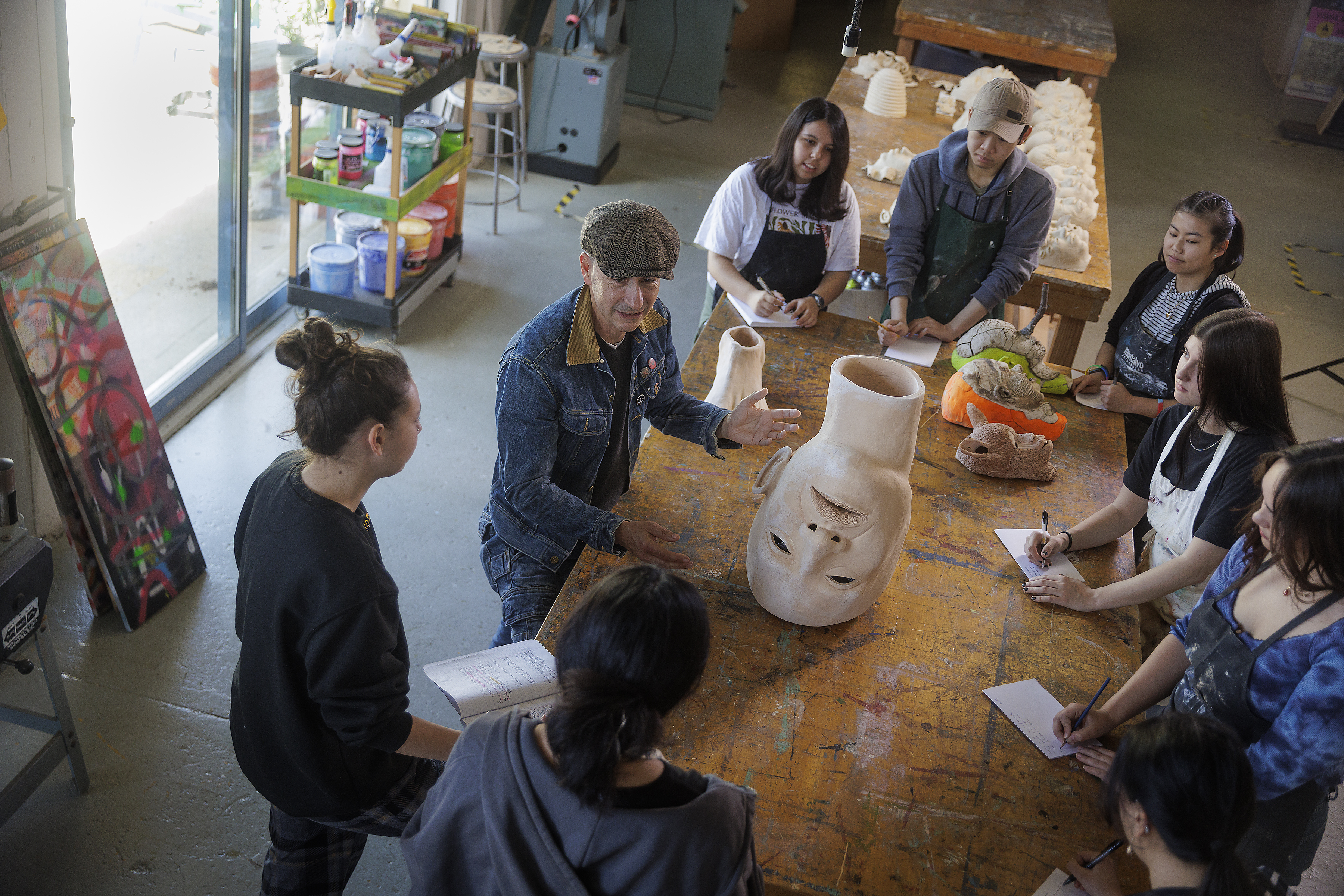 Group of students with instructor holding a pottery ceramic head during a sculpting class