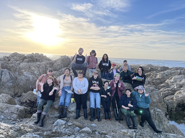 A group of students smiling and posing for the camera in front of a rocky intertidal pool system.