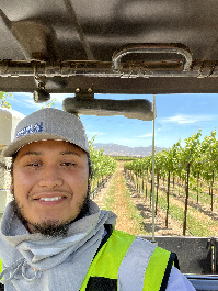 Adrian smiling with a vineyard behind him